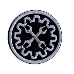 May include: A black and silver embroidered patch featuring a gear and wrench design. The patch is circular and has a white border.