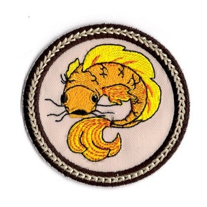 May include: Embroidered patch featuring a yellow and orange fish with a brown and beige border.