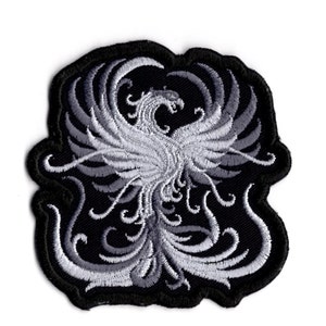 May include: Embroidered patch depicting a phoenix in grey and white on a black background. The patch has a detailed design with swirling patterns and a scalloped edge, suitable for clothing or accessories.