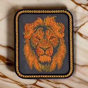May include: Embroidered lion head patch with a gold border. The lion is orange and yellow with a gray background.