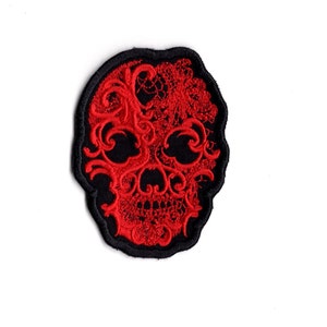 May include: Red embroidered skull patch with a black border. The skull is decorated with a lace-like design.