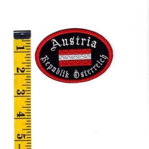 May include: A red, white, and black embroidered patch with the text "Austria Republik &Ouml;sterreich" in a gothic font. The patch features the Austrian flag in the center.