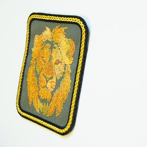 May include: A yellow embroidered lion head patch with a black and yellow border. The patch is on a white background.