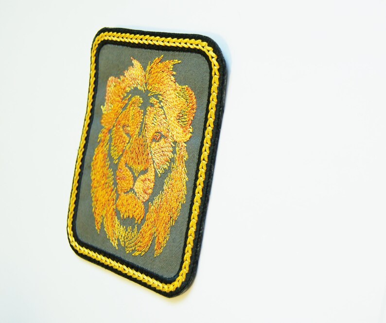 May include: A yellow embroidered lion head patch with a black and yellow border. The patch is on a white background.