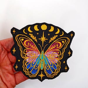May include: Embroidered iron-on patch featuring a colorful butterfly with a crescent moon and stars on a black background.