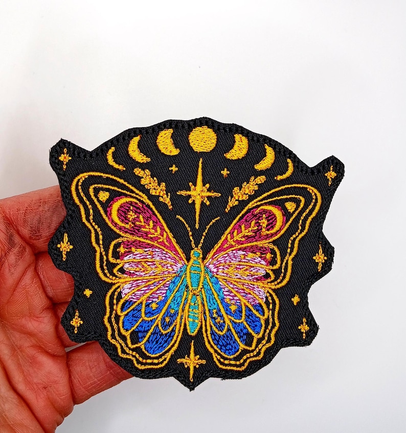 May include: Embroidered iron-on patch featuring a colorful butterfly with a crescent moon and stars on a black background.