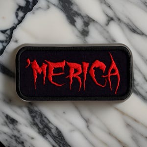 May include: A black rectangular patch with the word "MERICA" embroidered in red.