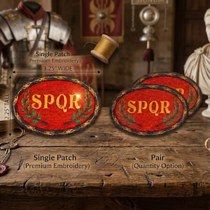 May include: Oval embroidered patch with the letters SPQR in gold on a red background, framed by a gold border and green laurel leaves. The patch is 3.25 inches wide and 2.25 inches tall. The image shows a single patch and a pair.