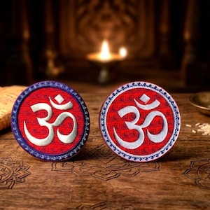 Peut inclure: Deux écussons ronds avec le symbole Om. Les écussons ont un fond rouge avec un symbole Om blanc et une bordure bleue et blanche. Ils sont posés sur une surface en bois.