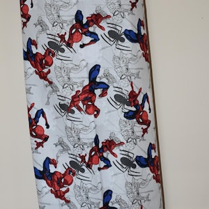 May include: White fabric with a repeating pattern of Spiderman in red and blue swinging from a web. The background is white with black outlines of Spiderman and webs.