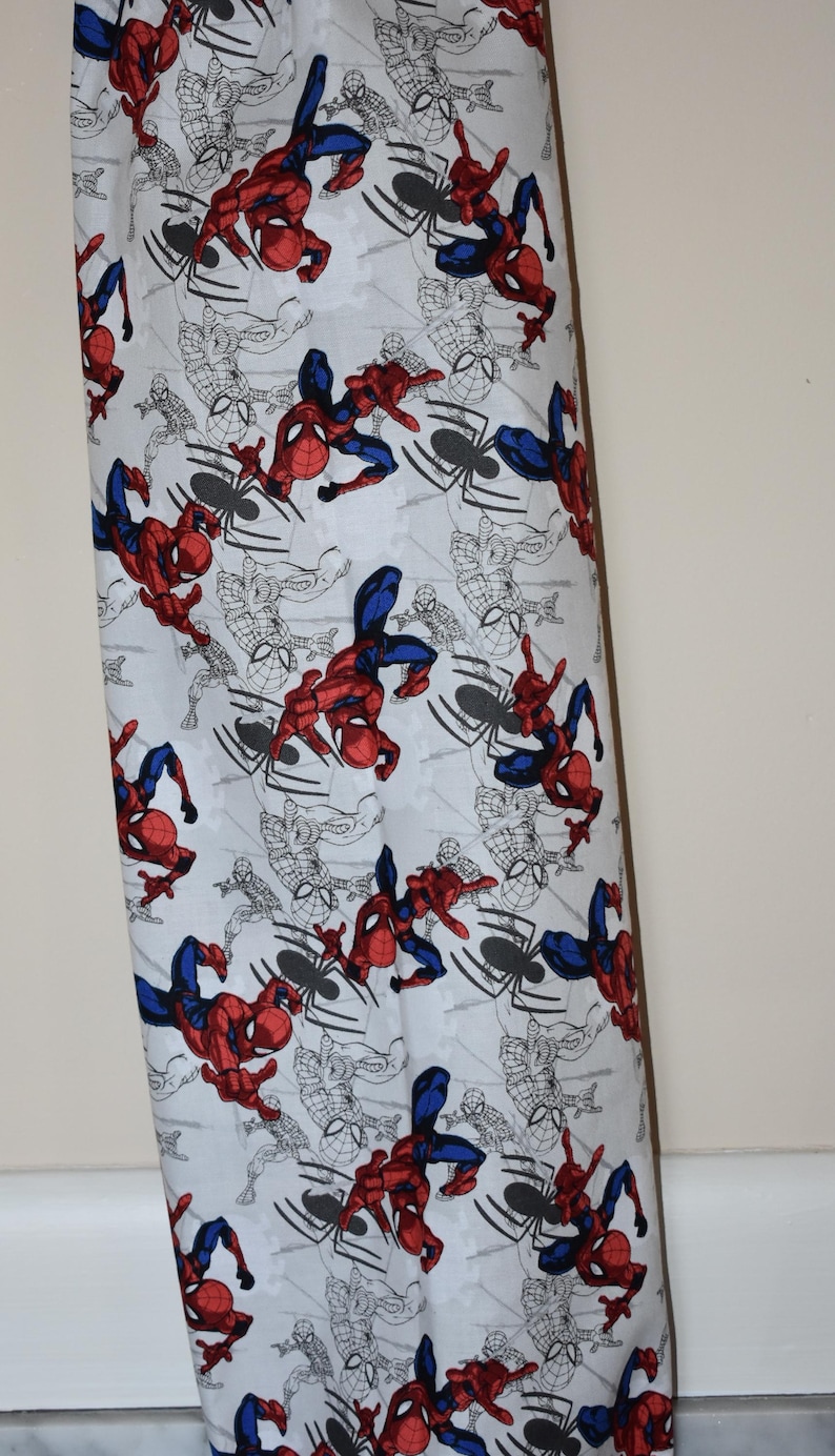 May include: White fabric with a repeating pattern of Spiderman in red and blue swinging from a web. The background is white with black outlines of Spiderman and webs.