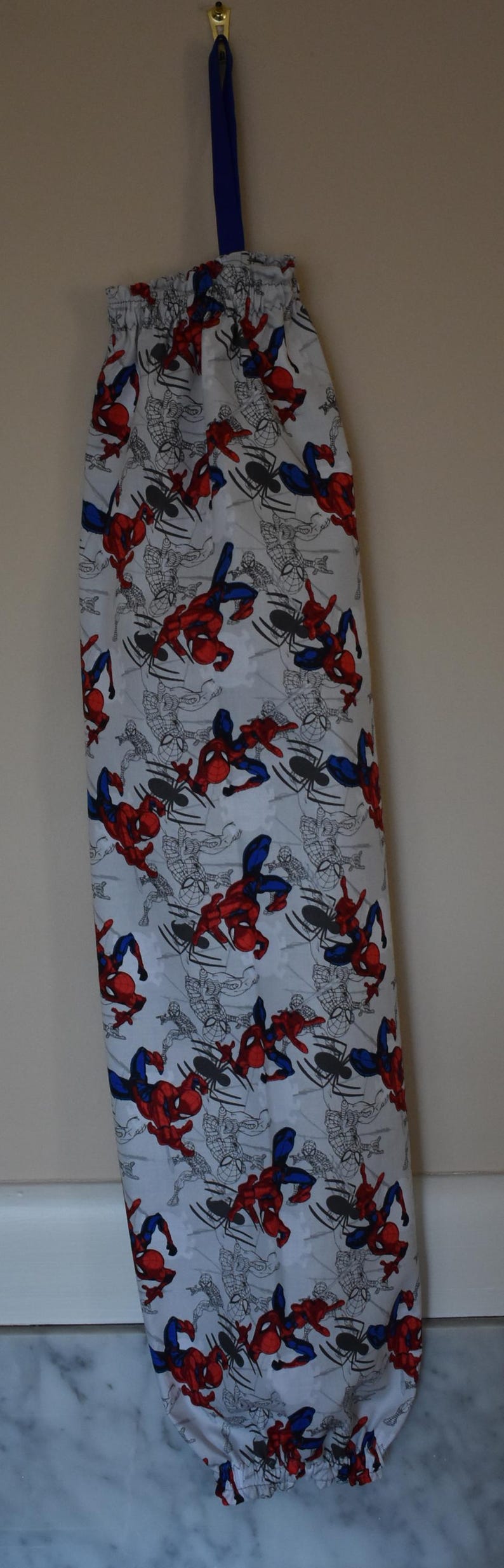 May include: A white reusable grocery bag with a blue drawstring and a pattern of red and blue Spiderman characters on a white background.