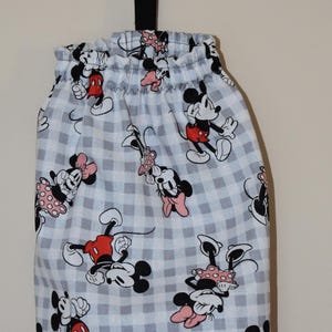 May include: A white and gray gingham fabric trash bag holder with a black hanging loop. The fabric features a repeating pattern of Mickey Mouse and Minnie Mouse in red, black, and white.