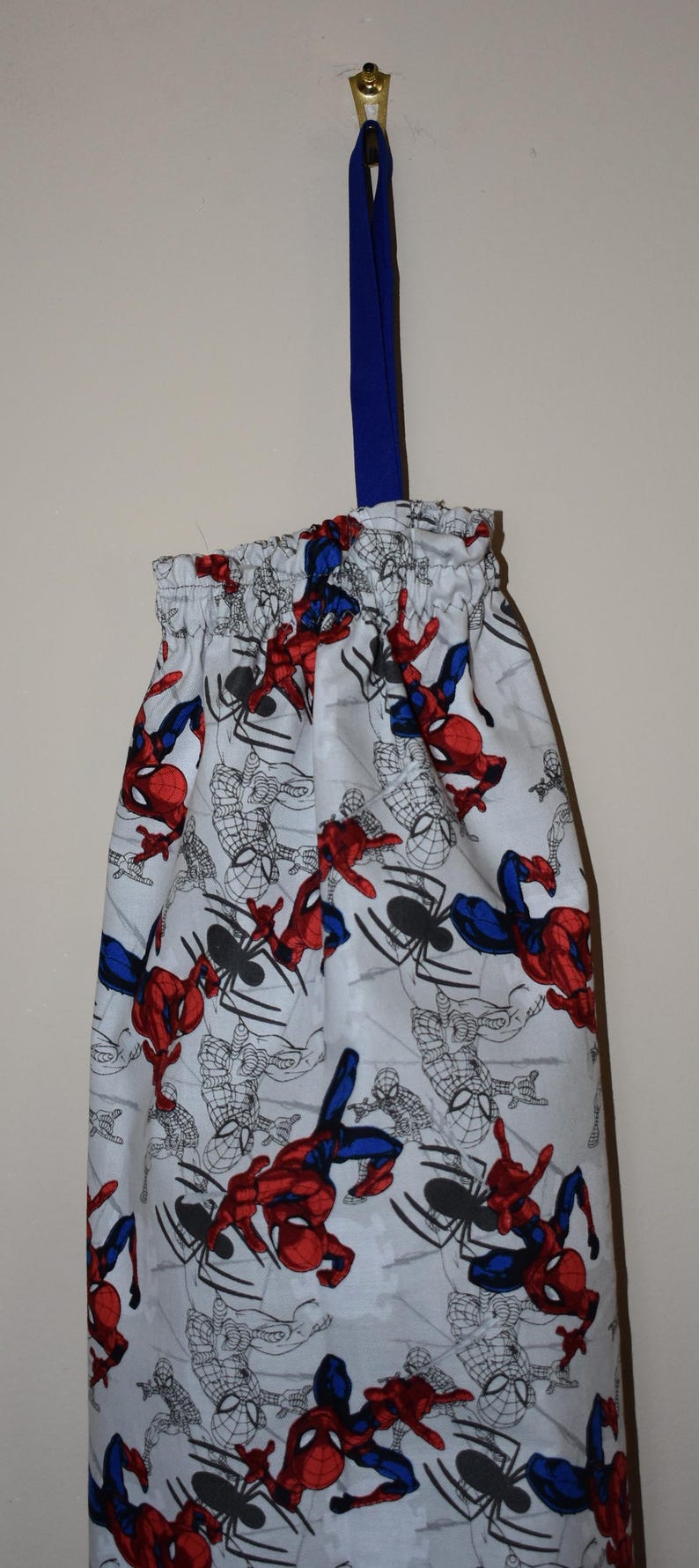 May include: A white drawstring bag with a blue strap. The bag is decorated with a repeating pattern of Spiderman characters in red, blue, and black.