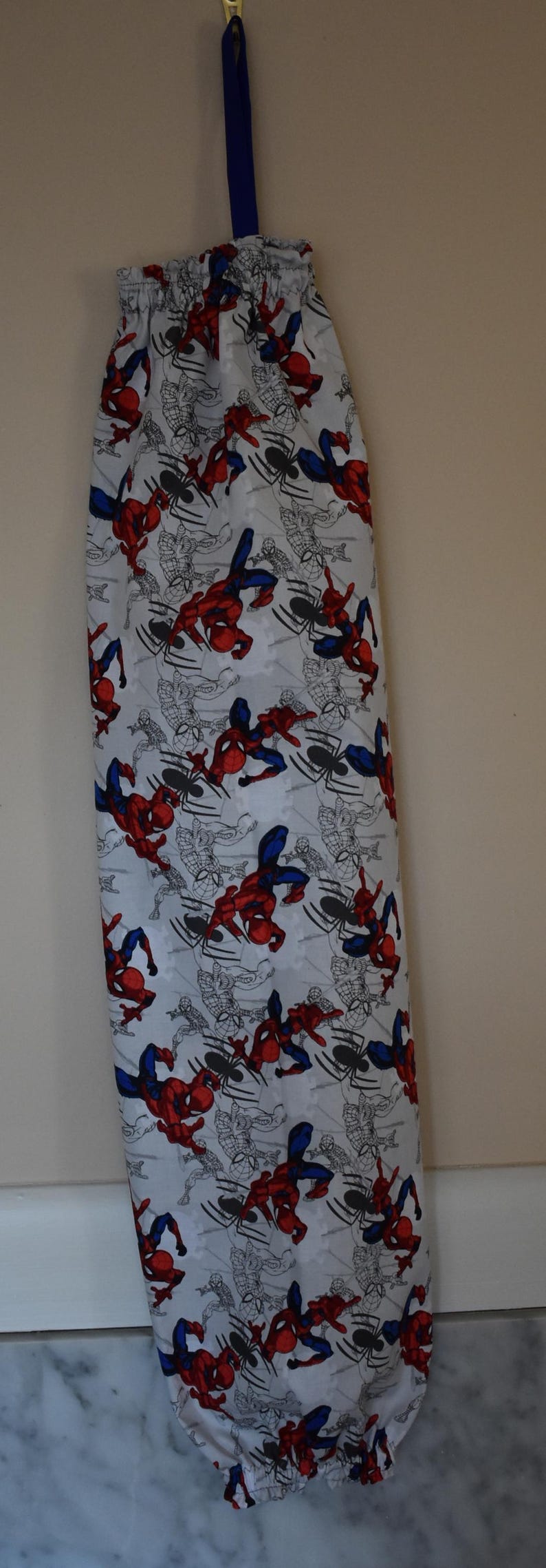 May include: A white reusable grocery bag with a blue drawstring and a pattern of red and blue Spiderman characters on a white background.