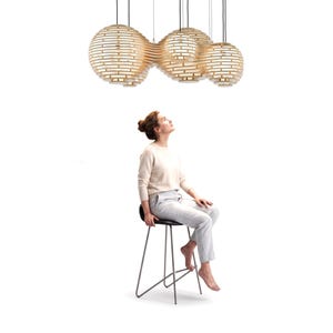 May include: A large, multi-spherical pendant light fixture constructed from light-colored, horizontal wooden slats. The fixture features several interconnected, globe-shaped sections of varying sizes, suspended by thin black cords from above.