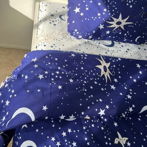 K&ouml;nnte beinhalten: Ein blaues und wei&szlig;es Bettw&auml;sche-Set mit einem Sternen- und Halbmondmuster. Die Bettw&auml;sche ist aus weichem, bequemem Stoff gefertigt und perfekt, um jedem Schlafzimmer einen Hauch von Verspieltheit zu verleihen.