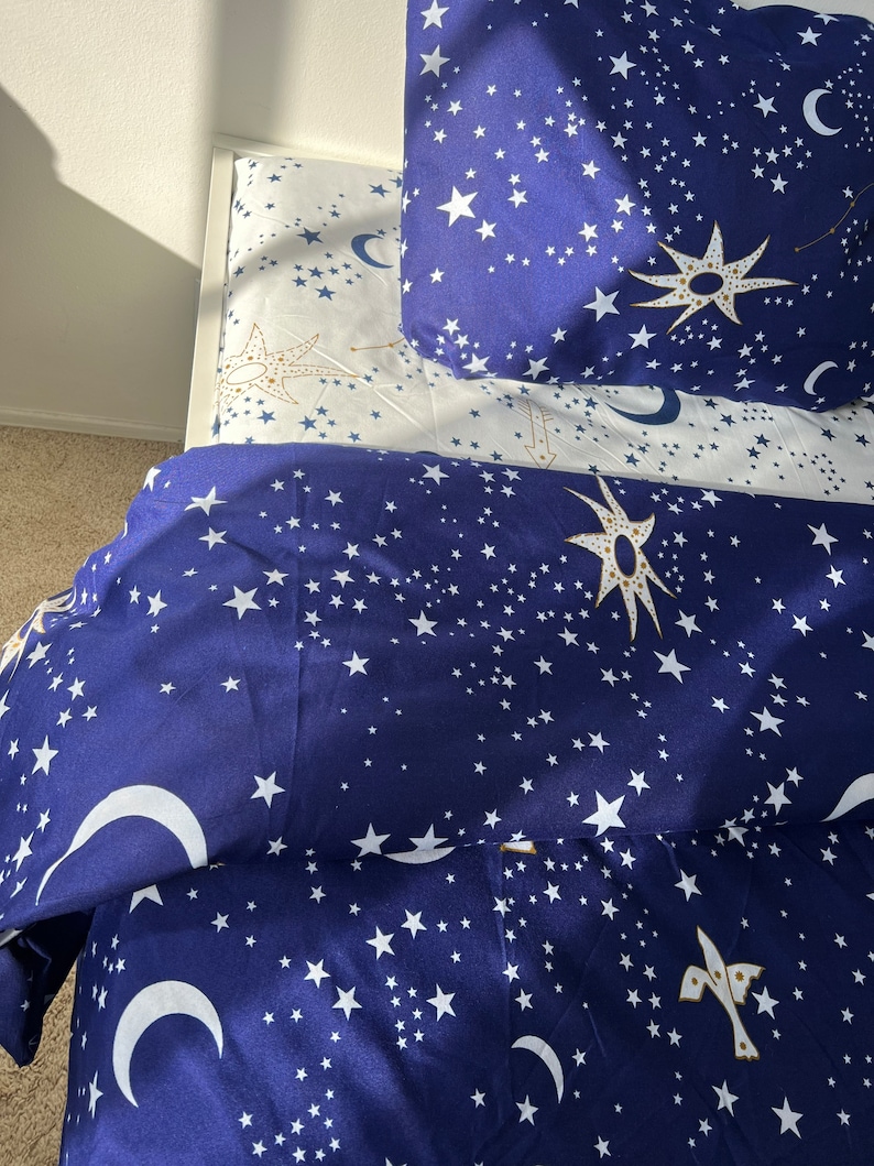 K&ouml;nnte beinhalten: Ein blaues und wei&szlig;es Bettw&auml;sche-Set mit einem Sternen- und Halbmondmuster. Die Bettw&auml;sche ist aus weichem, bequemem Stoff gefertigt und perfekt, um jedem Schlafzimmer einen Hauch von Verspieltheit zu verleihen.