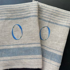 Könnte beinhalten: Zwei Leinen-Geschirrtücher mit blauen Streifen und einem blauen gestickten Buchstaben "O" auf jedem.