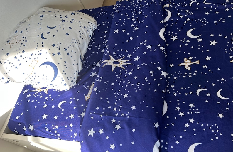 K&ouml;nnte beinhalten: Blaue Bettw&auml;sche mit einem Muster aus wei&szlig;en Sternen und Halbmonden. Die Bettw&auml;sche ist aus einem weichen, bequemen Stoff gefertigt und perfekt f&uuml;r ein Kinderzimmer.