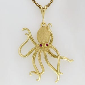 Peut inclure: Un collier pendentif en or représentant un poulpe. Le pendentif présente un design de poulpe avec des yeux en pierres précieuses rouges. Le collier est suspendu à une fine chaîne en or. Le poulpe a huit tentacules incurvées.