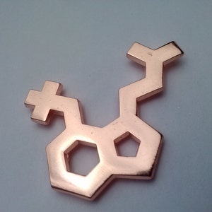 May include: A rose gold metal pendant shaped like a chemical molecule. The pendant is a geometric design with a hexagonal shape in the center.