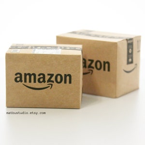 May include: Two brown cardboard boxes with the Amazon logo printed on them. The boxes are stacked on top of each other.