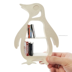 May include: White penguin-shaped bookshelf with two shelves. The bookshelf is holding a variety of books.