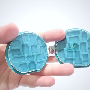 May include: A teal blue silicone mould with multiple shapes for making miniature objects. The mould is open and shows the inside of the mould.