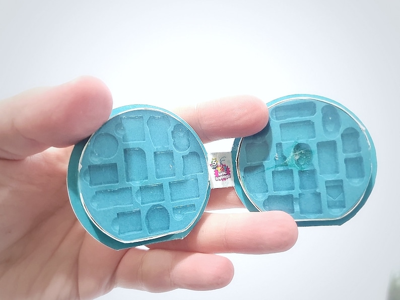 May include: A teal blue silicone mould with multiple shapes for making miniature objects. The mould is open and shows the inside of the mould.
