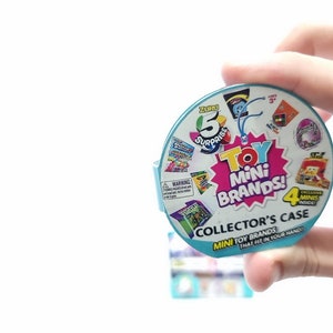 May include: A blue and white round plastic container with the words "ZURU 5 Surprise Toy Mini Brands! Collector's Case Mini Toy Brands That Fit In Your Hand!" printed on it. The container has a clear plastic window showing a variety of small toys inside.