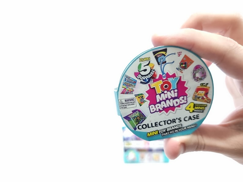 May include: A blue and white round plastic container with the words "ZURU 5 Surprise Toy Mini Brands! Collector's Case Mini Toy Brands That Fit In Your Hand!" printed on it. The container has a clear plastic window showing a variety of small toys inside.