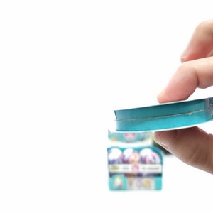 May include: A roll of teal blue ribbon with a white core. The ribbon is being held by a hand.