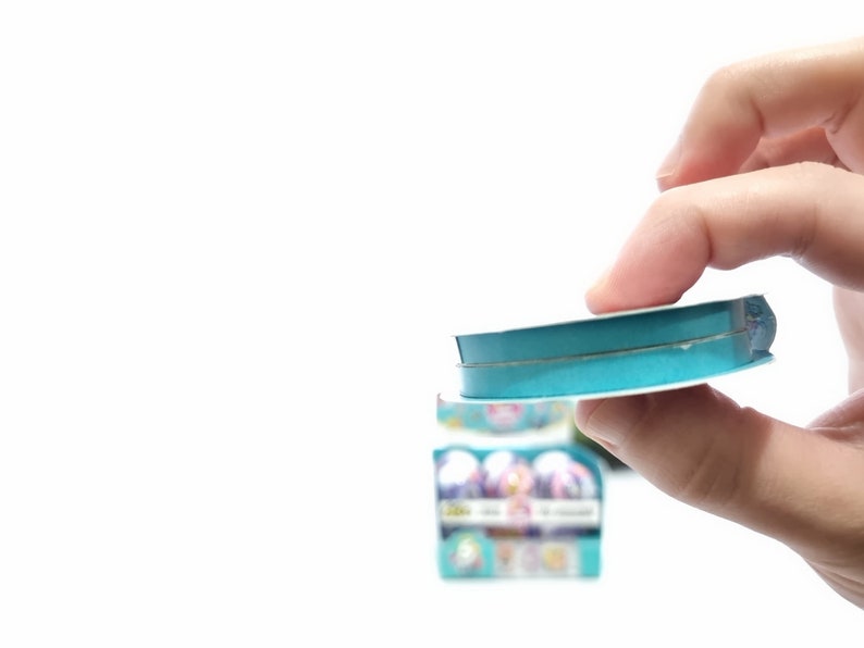 May include: A roll of teal blue ribbon with a white core. The ribbon is being held by a hand.