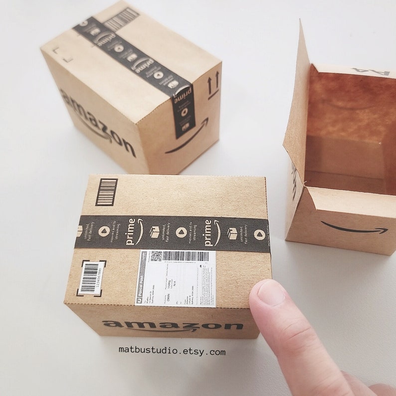 May include: Three brown cardboard boxes with the Amazon logo and Prime branding. The boxes are different sizes and one is open. The text on the box reads "amazon" and "matbustudio.etsy.com".