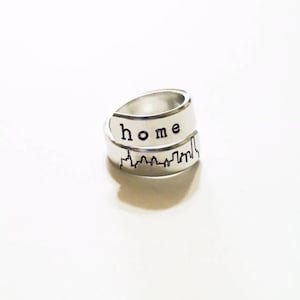 May include: A silver ring with a cityscape design and the word "home" engraved on the band.