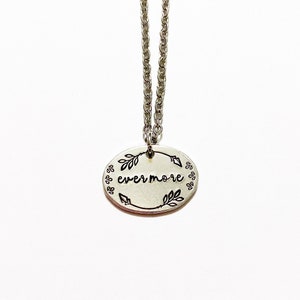 May include: Silver necklace with a round pendant that says "evermore" with arrows and leaves around the word.