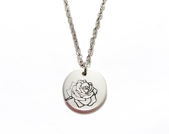 May include: A silver necklace with a round pendant featuring a delicate engraved rose design.