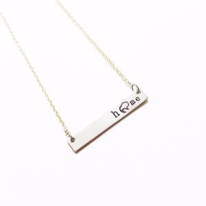 May include: A silver necklace with a bar pendant that says "home" with a small buffalo silhouette above the word.