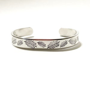 May include: A silver metal bracelet with a design of leaves etched into the surface.