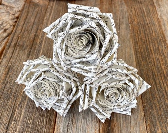 May include: Three white paper roses made from the pages of a book. The roses are arranged in a cluster on a wooden surface.