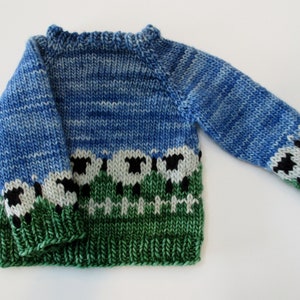 May include: A blue and green knitted sweater with a sheep pattern. The sweater has a crew neck and long sleeves.