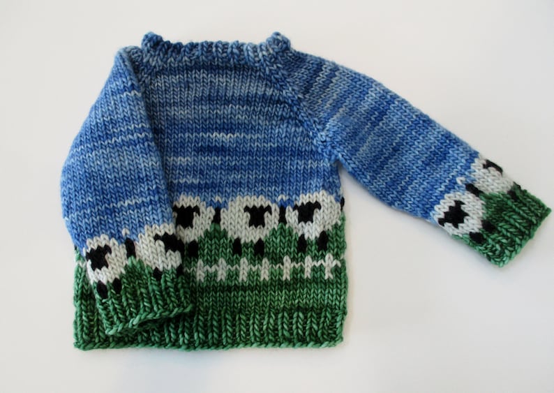 May include: A blue and green knitted sweater with a sheep pattern. The sweater has a crew neck and long sleeves.