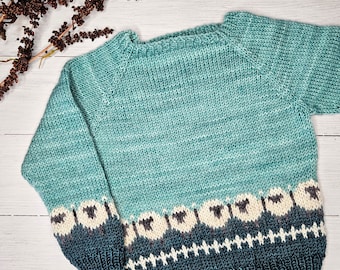 May include: A teal blue knitted sweater with a white and black sheep pattern on the bottom hem.