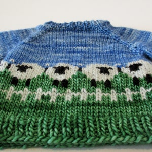 May include: A blue, green, and white knitted sweater with a pattern of sheep in a field.