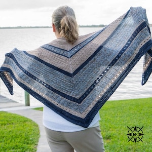 May include: A blue, brown, and white knitted shawl with a lacy border. The shawl is draped over the shoulders of a person standing outdoors.