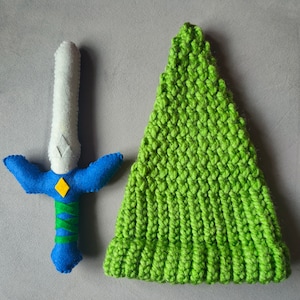 May include: A green knitted hat and a blue and white felt sword with a yellow triangle design.