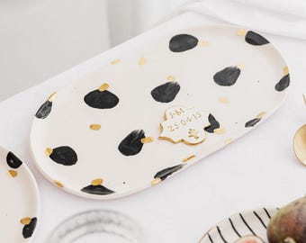 May include: White oval ceramic serving tray with black and gold abstract spots. The tray has a small gold plaque with the text "J&M 25-04-15" on it.