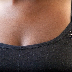 May include: A black tank top with a silver spider pin on the strap.