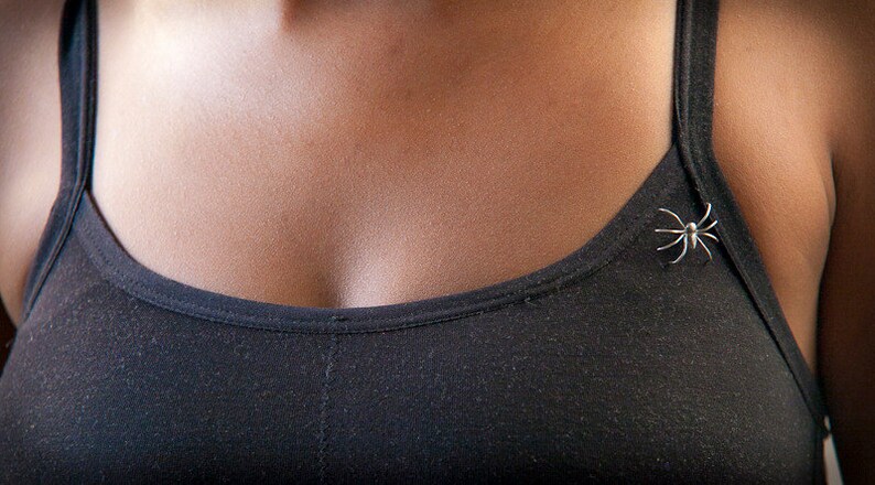 May include: A black tank top with a silver spider pin on the strap.